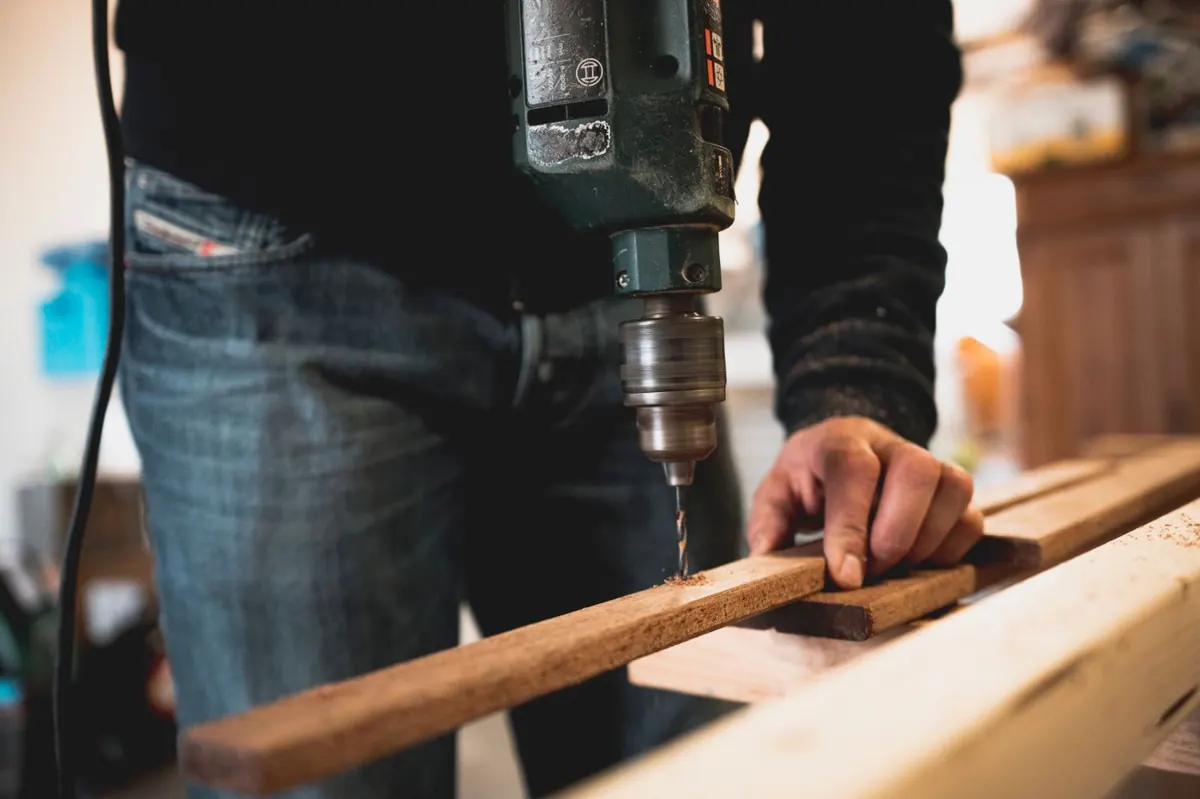 Perçage sur établi, planche, perceuse, jeans de travail.